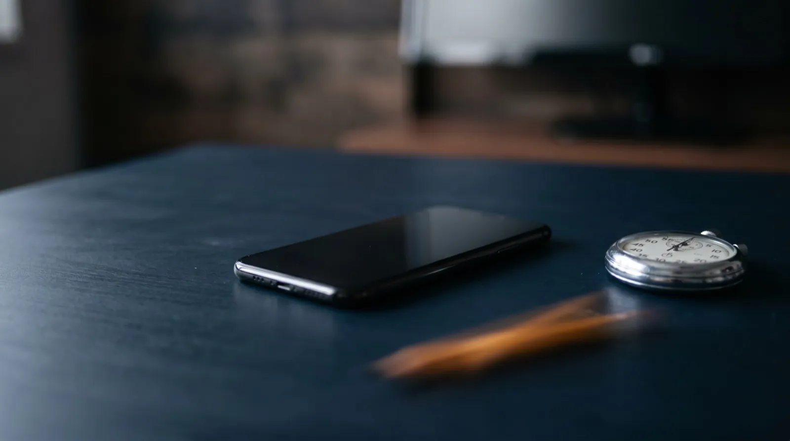 A smartphone resting on a dark navy desk beside a stopwatch in natural light, no people